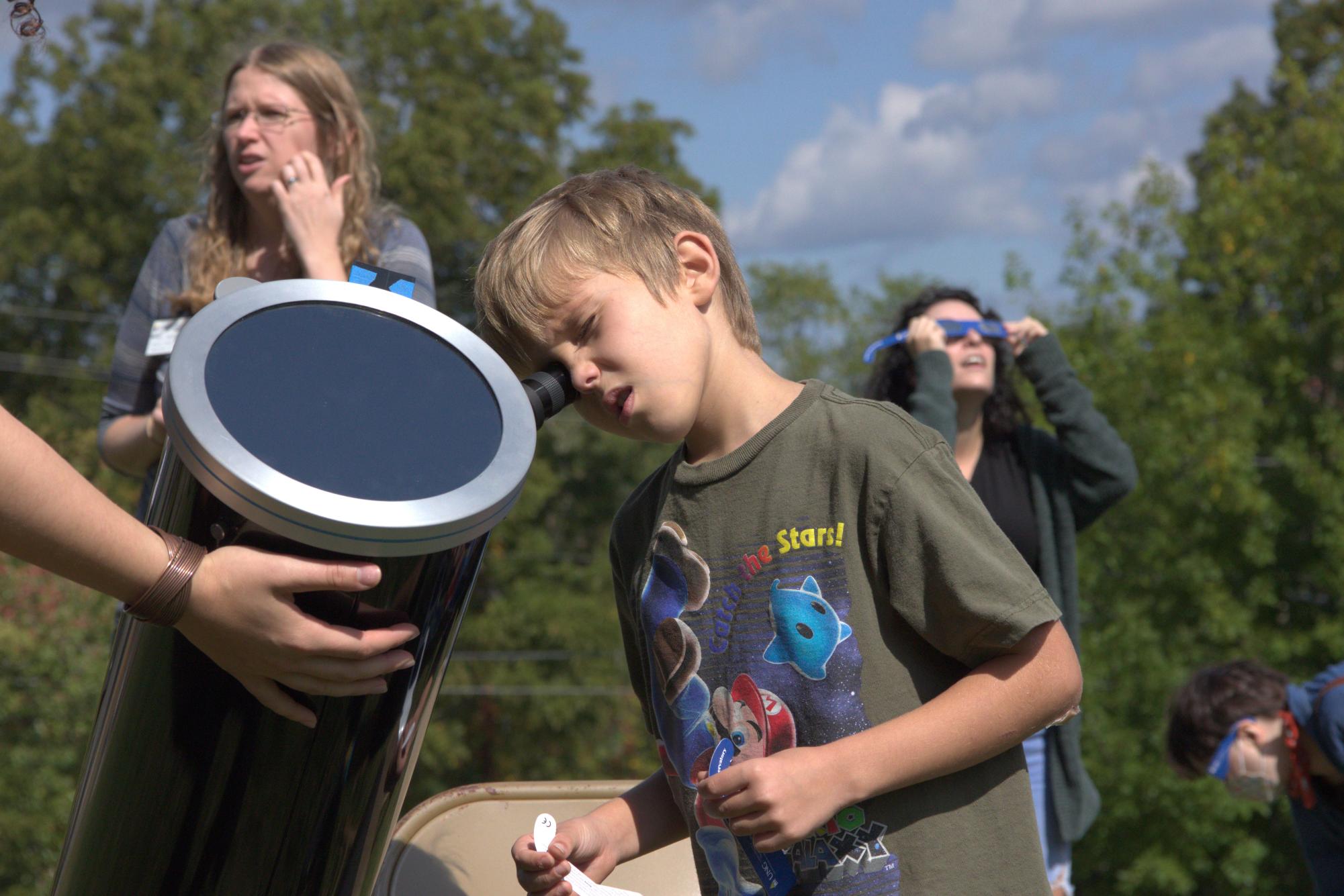 A young visitor views the eclipse through a telescope.